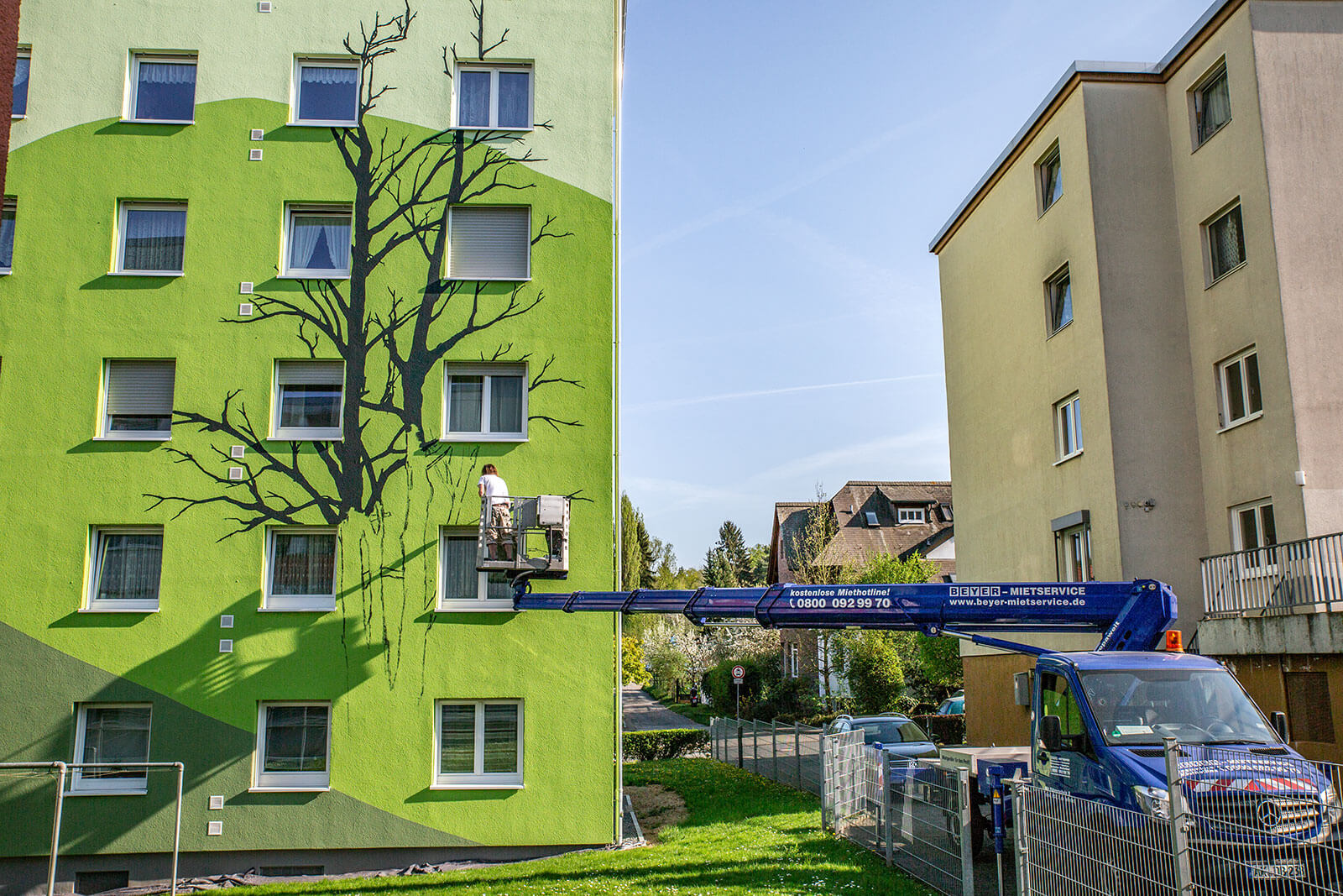 27 m LKW-Steiger auf 3,5 to Fahrgestell unterstützt Malerarbeiten an Fassade durch Übergreifen von Zaun