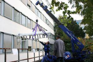 Abgestützter Minikran beim Lastentransport vor Gebäude