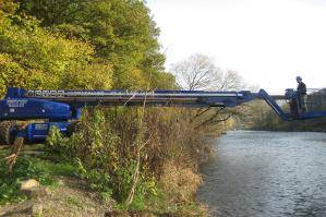 Teleskoparbeitsbühne von der Seite mit ausgefahrenem Teleskoparm über Fluss